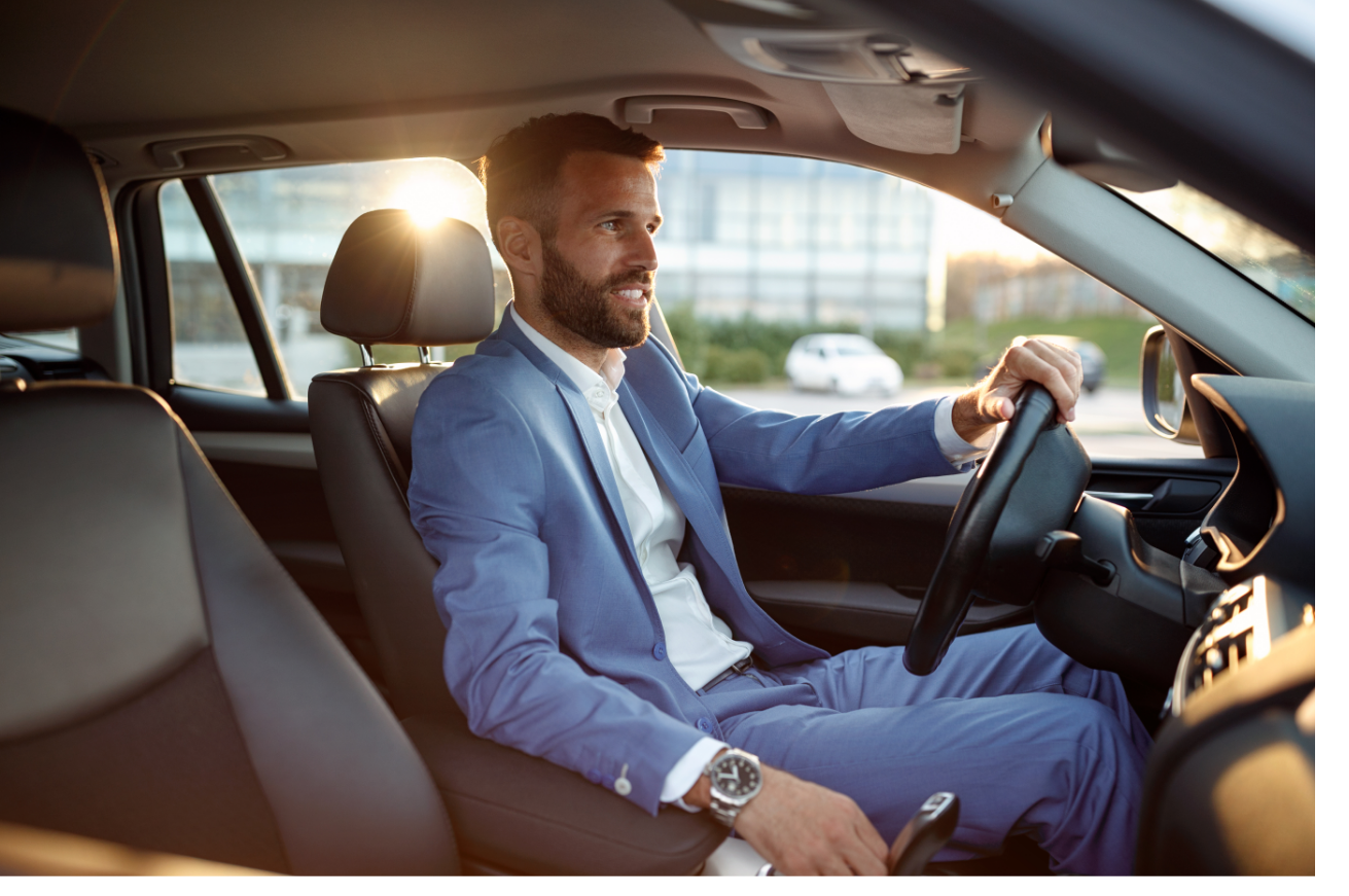 A man in a suit is sitting in the driver 's seat of a car.