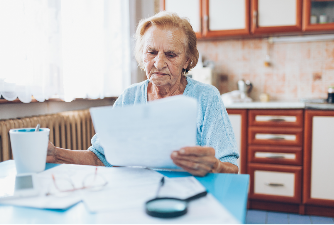 An elderly woman is sitting at a table reading a piece of paper.