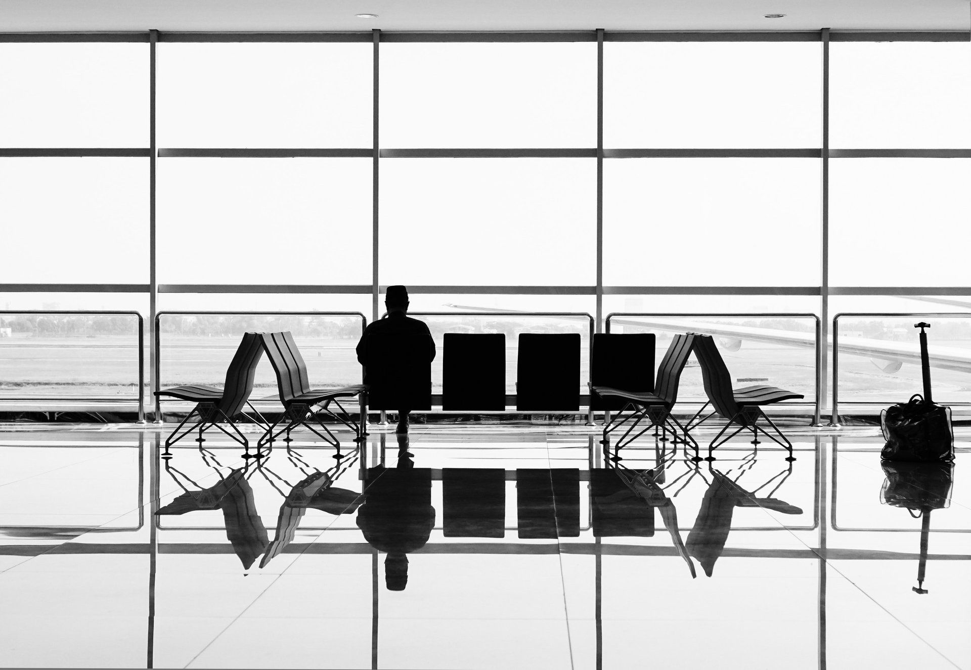 A black and white photo of a man sitting in an airport waiting area.