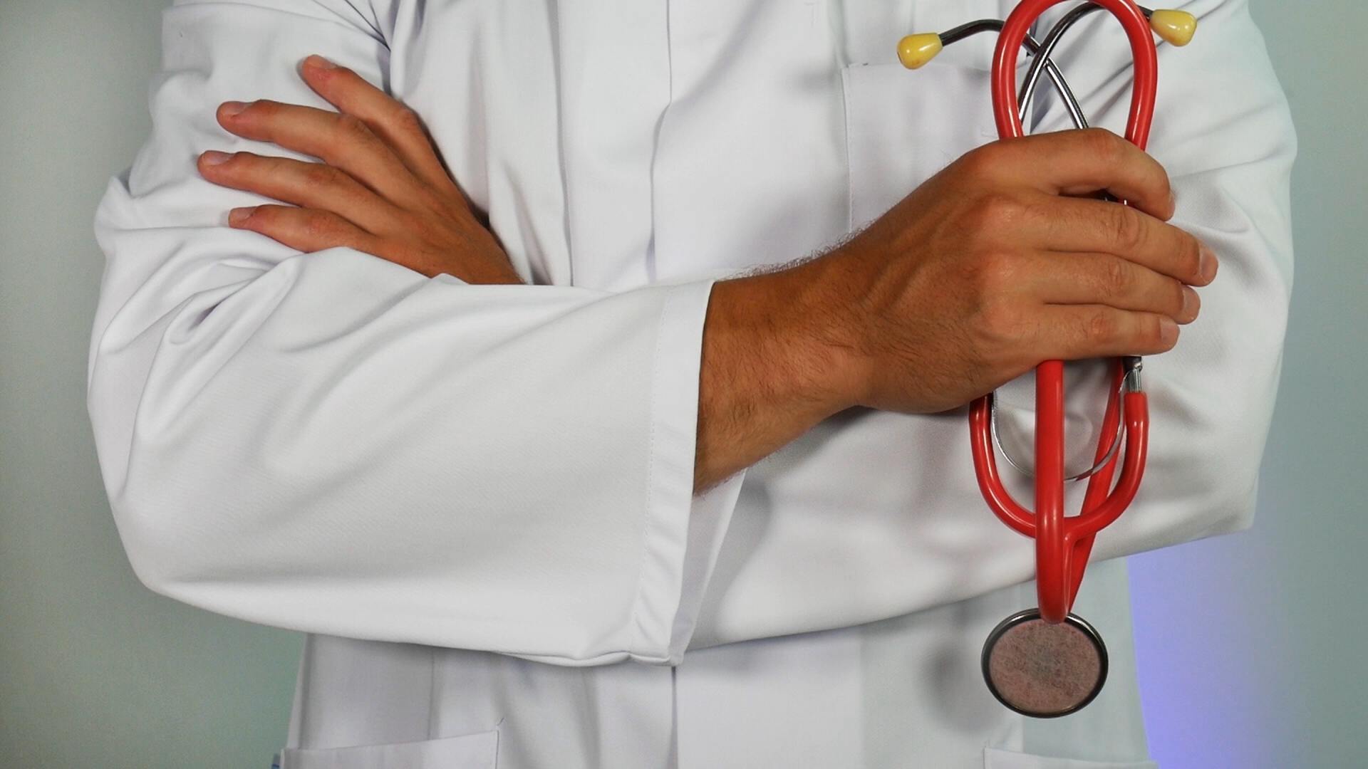 A doctor is holding a red stethoscope around his neck.