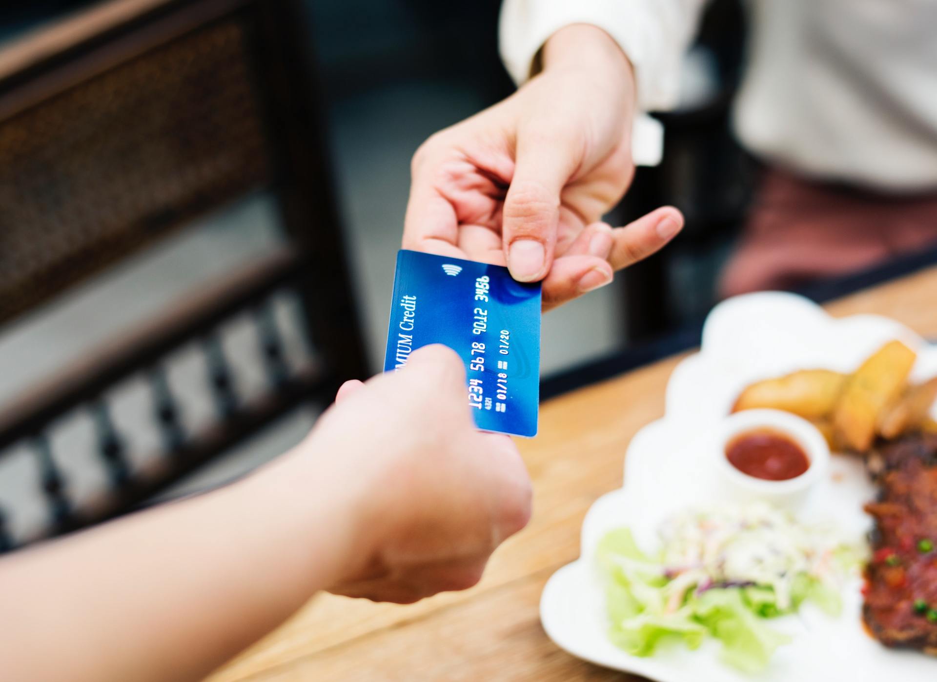 A person is handing a credit card to another person in front of a plate of food.