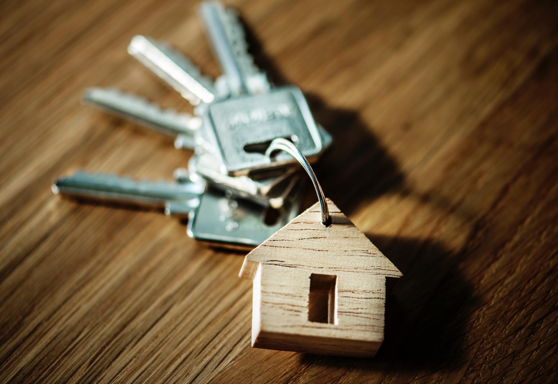 A bunch of keys with a wooden house keychain on a wooden table.