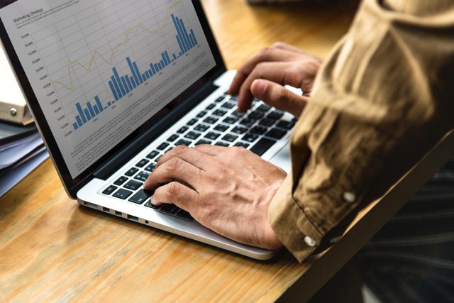 A person is typing on a laptop computer with a graph on the screen.