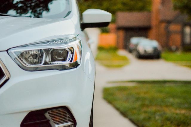 A white car is parked on the side of the road in front of a house.