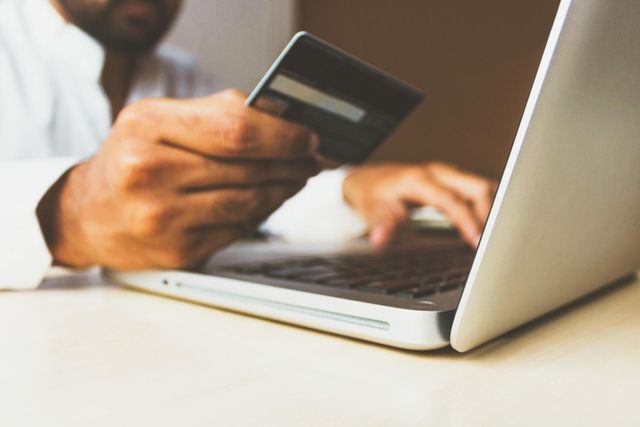 A man is holding a credit card while typing on a laptop