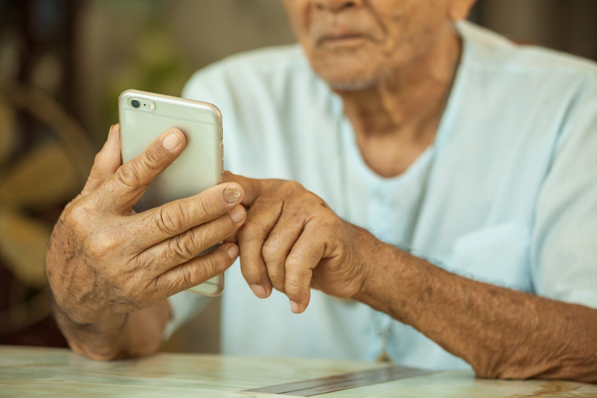 An elderly man is sitting at a table using a cell phone.